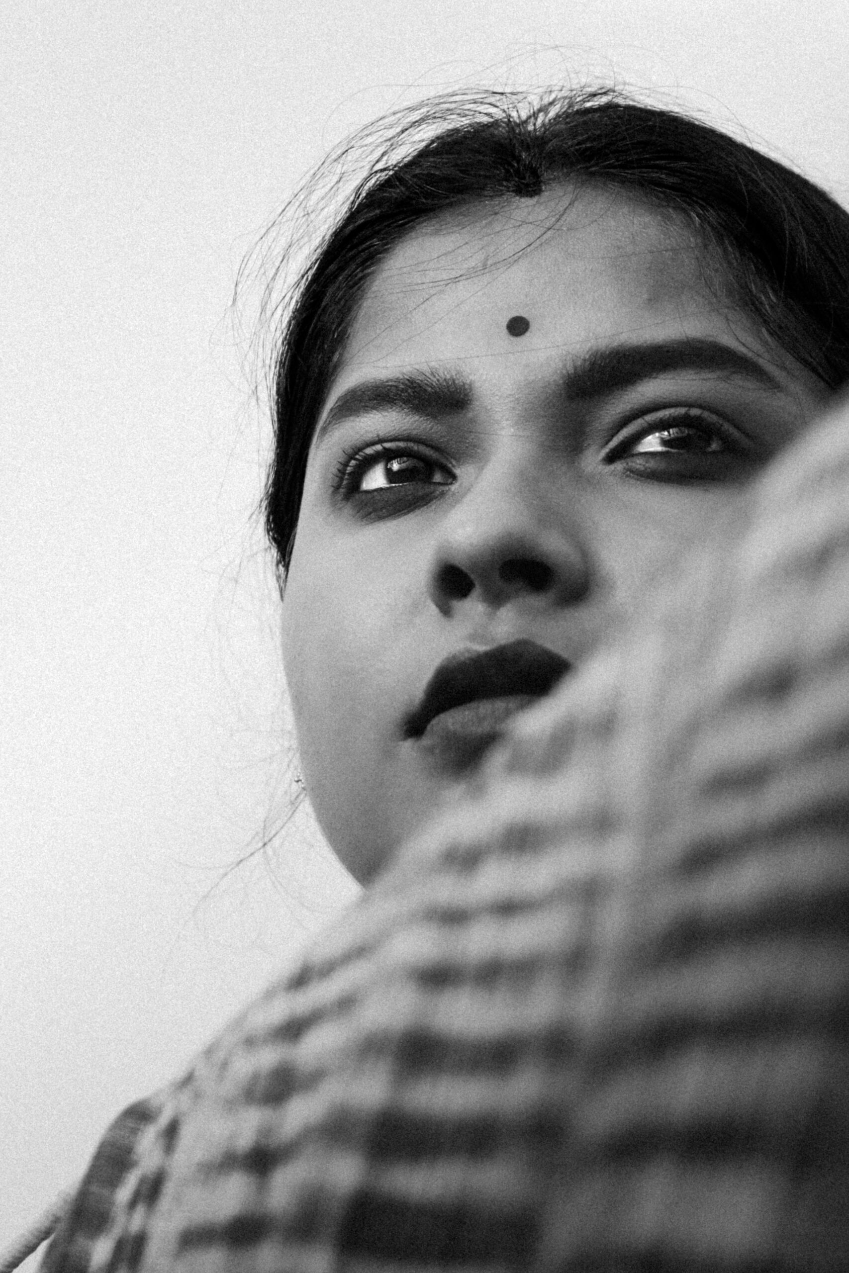 Close-up black and white portrait of a woman with a bindi, conveying a thoughtful expression.